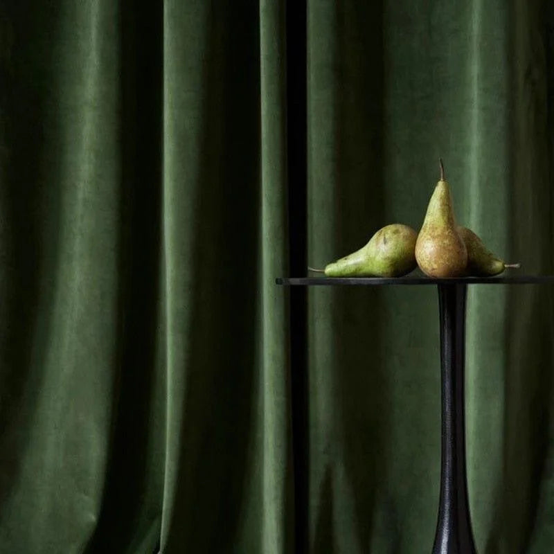 Rideau vert foncé élégant avec table noire moderne et trio de poires, décoration intérieure sophistiquée.