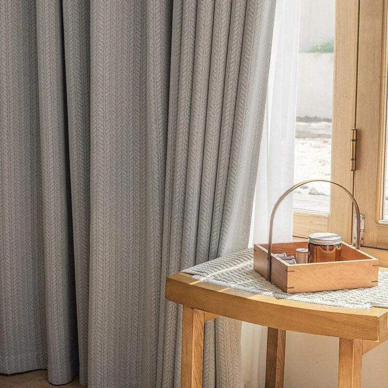 Rideau gris élégant suspendu dans un salon éclairé par la lumière naturelle, complété par une table en bois avec un plateau et des accessoires pour une ambiance confortable et accueillante.