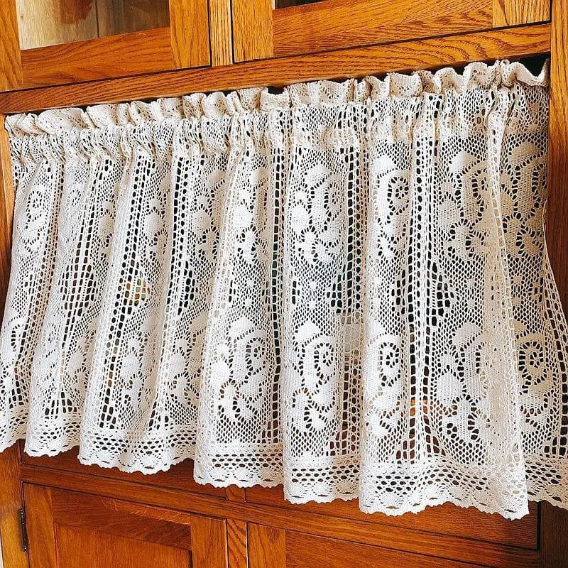 Rideau blanc décoratif au style vintage avec motifs floraux ajourés, idéal pour embellir une cuisine ou une salle à manger. Fixé sur une tringle en bois, il offre une touche d'élégance et de lumière douce à votre intérieur. Accessoire parfait pour un aménagement de maison chaleureux et classique.