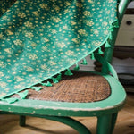 Chaise en bois vert avec une couverture verte décorée de motifs festifs dorés, ornée de franges. Idéale pour ajouter une touche de style à votre décoration intérieure, parfaite pour les espaces de vie chaleureux.