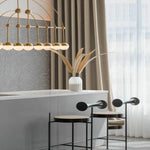 Salle à manger moderne avec suspensions élégantes et tabourets minimalistes noirs. Décoration contemporaine mise en valeur par un éclairage raffiné et un vase avec des branches décoratives. Design intérieur chic et épuré.