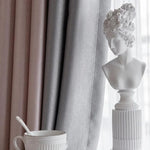Buste blanc élégant sur fond de rideaux crème et gris, décoration intérieure raffinée, parfaite pour ajouter une touche artistique et sophistiquée à votre espace de vie. Accompagnez votre décor d'une tasse de café stylisée pour un moment de détente impeccablement chic.