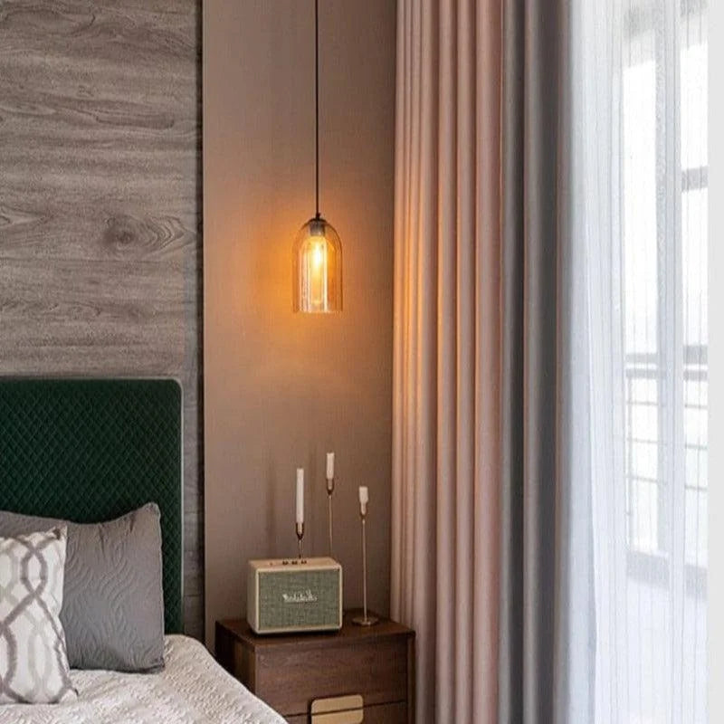 Chambre moderne et élégante avec suspension lumineuse au-dessus d'une table de chevet en bois. Cette décoration intérieure crée une ambiance chaleureuse grâce à un éclairage tamisé. Les rideaux ajoutent une touche de sophistication à la pièce, tandis que le lit avec tête de lit rembourrée et coussins assortis offre confort et style. Parfait pour une atmosphère apaisante et contemporaine.