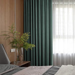 Chambre moderne avec rideaux opaques verts et voilages pour une ambiance chaleureuse. Lit confortable avec draps élégants et table de chevet en bois. Décoration naturelle avec plante verte dans un vase transparent, offrant une touche apaisante et design. Luminosité douce grâce à la lumière filtrée par les rideaux. Idéale pour une décoration intérieure contemporaine.