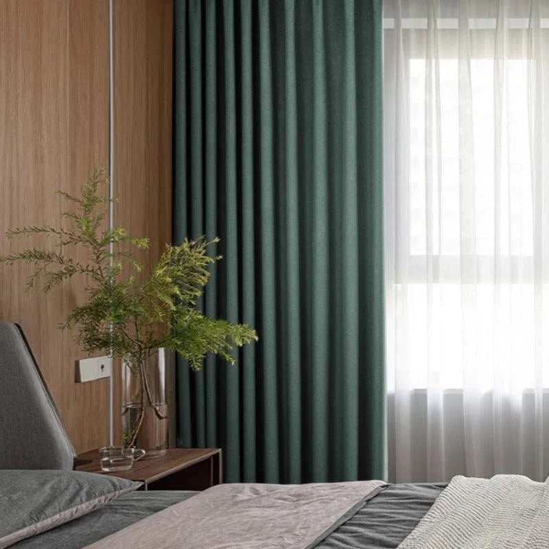 Chambre moderne avec rideaux opaques verts et voilages pour une ambiance chaleureuse. Lit confortable avec draps élégants et table de chevet en bois. Décoration naturelle avec plante verte dans un vase transparent, offrant une touche apaisante et design. Luminosité douce grâce à la lumière filtrée par les rideaux. Idéale pour une décoration intérieure contemporaine.