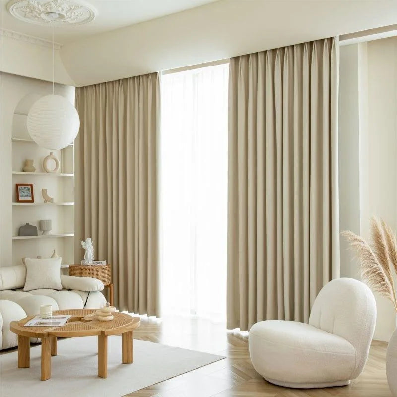 Salon élégant avec rideaux beiges, canapé moderne et décoration harmonieuse. Luminosité et design dans un intérieur contemporain. Espace détente avec fauteuil confortable et table basse en bois. Atmosphère apaisante et style minimaliste.