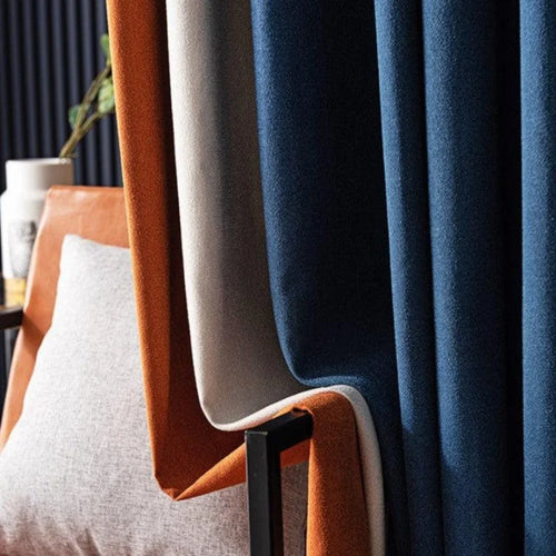 Rideaux modernes bleus et orange suspendus, créant un contraste élégant dans un intérieur sophistiqué, avec un coussin gris clair en arrière-plan. Solution idéale pour ajouter une touche de couleur et de style contemporain à votre salon ou chambre.