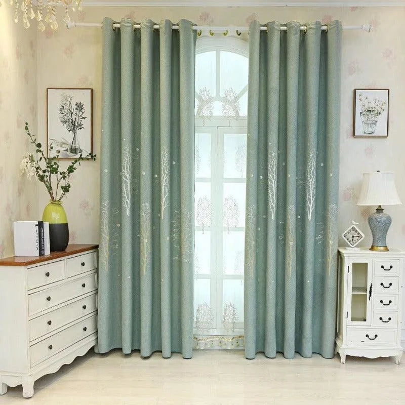 Rideaux élégants bleu-vert avec motifs d'arbres, suspendus dans un salon lumineux et décoré avec goût. Mobilier classique et accessoires décoratifs raffinés complètent cet intérieur accueillant. Idéal pour apporter une ambiance naturelle et apaisante à votre espace de vie.