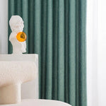 Buste décoratif moderne posée sur une table blanche, avec des rideaux texturés verts en arrière-plan et une chaise contemporaine arrondie, créant un intérieur élégant et artistique.