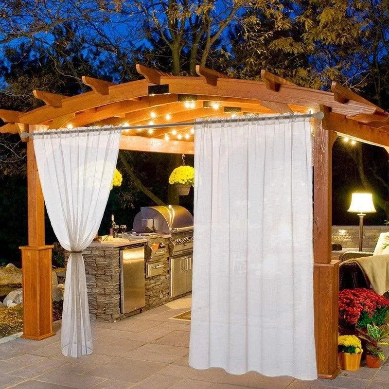 Pergola de jardin élégante éclairée, avec rideaux blancs offrant intimité et charme. Parfait pour les repas en plein air et les soirées conviviales. Aménagement extérieur avec éclairage chaleureux et espace barbecue intégré. Accessoire idéal pour embellir votre espace extérieur et créer une ambiance confortable et accueillante.