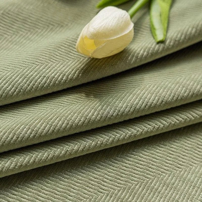 Image d'un tissu vert à motif chevron, accompagné d'une tulipe blanche posée délicatement dessus. Le décor floral complète le design élégant du textile, parfait pour une décoration intérieure moderne et apaisante. Accessoire idéal pour couvrir un canapé, un fauteuil ou ajouter une touche de sophistication à votre espace de vie.
