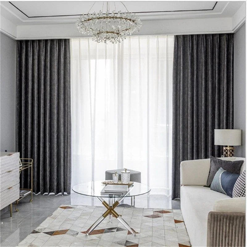 Salon élégant avec rideaux gris et voilage blanc, table basse ronde et tapis géométrique, idéal pour une décoration moderne et chic. Confort optimal avec canapé beige et coussins décoratifs, éclairé par un lustre raffiné.