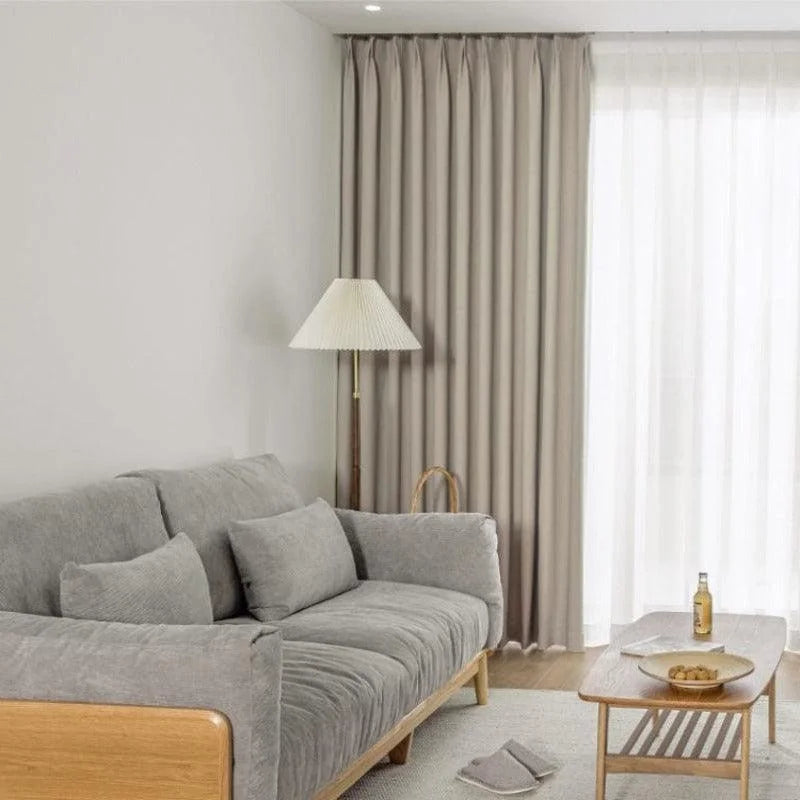 Salon moderne avec canapé gris, lampadaire élégant, table basse en bois, rideaux beiges et décoration minimaliste. Idéal pour un intérieur chaleureux et contemporain.