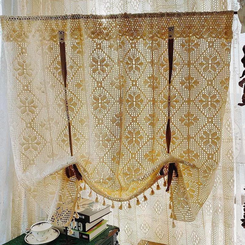 Rideau ajouré beige avec motif floral suspendu devant une fenêtre. Il décore élégamment un espace lumineux, appendi au-dessus de livres et d'une tasse de thé, créant une ambiance chaleureuse et accueillante. Parfait pour ajouter une touche romantique et rustique à tout intérieur.