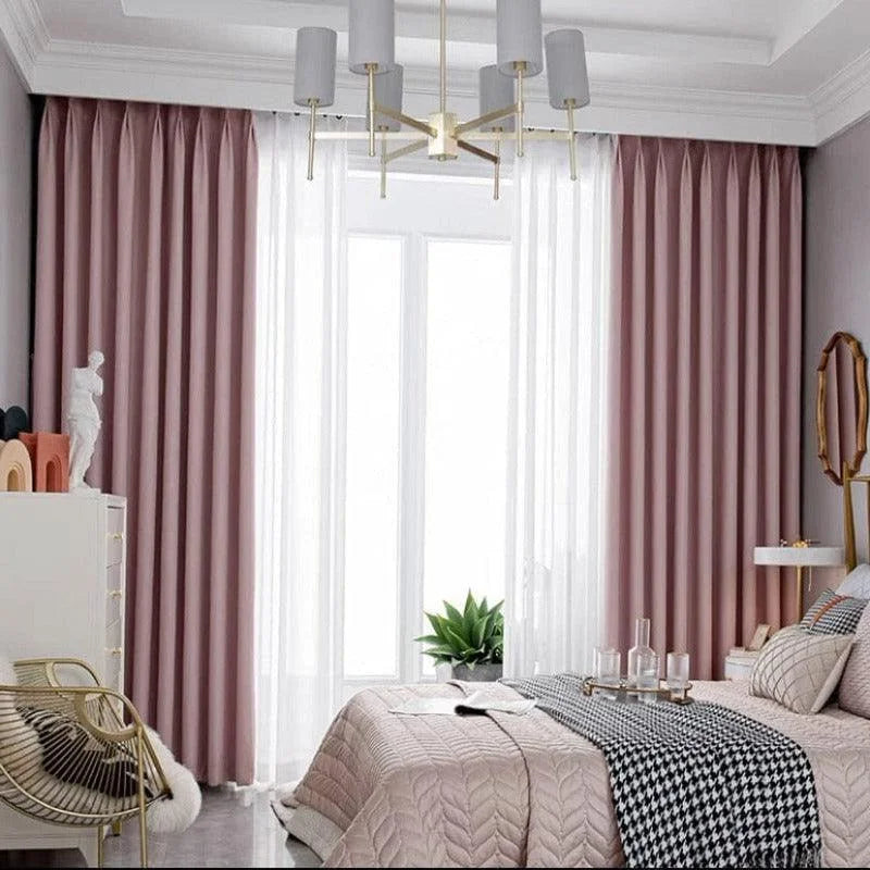 Chambre élégante décorée avec des rideaux rose pastel apportant une ambiance chaleureuse et cocooning. Le design moderne met en valeur une literie douce et accueillante, complétée par un éclairage sophistiqué et des détails décoratifs raffinés. Une plante verte près de la fenêtre ajoute une touche de fraîcheur à cet espace harmonieux.