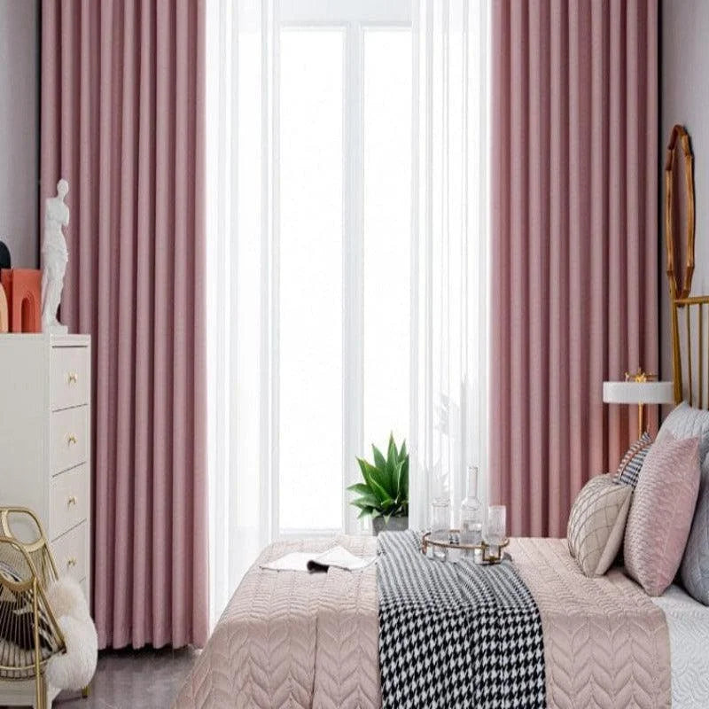 Chambre élégante avec rideaux rose poudré, offrant une ambiance chaleureuse et sophistiquée. La décoration harmonieuse se compose d'un lit confortable avec des coussins assortis, d'une plante verte apportant une touche naturelle et de mobilier moderne. Idéal pour un intérieur contemporain et raffiné.