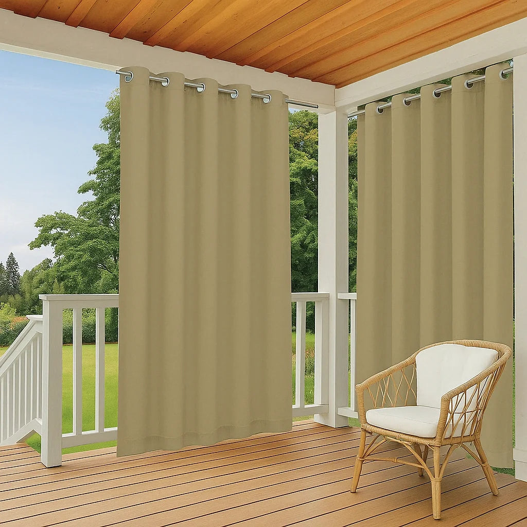 Rideaux d’extérieur beige clair à œillets installés sur une terrasse en bois, entourée de verdure et meublée d’un fauteuil en rotin.