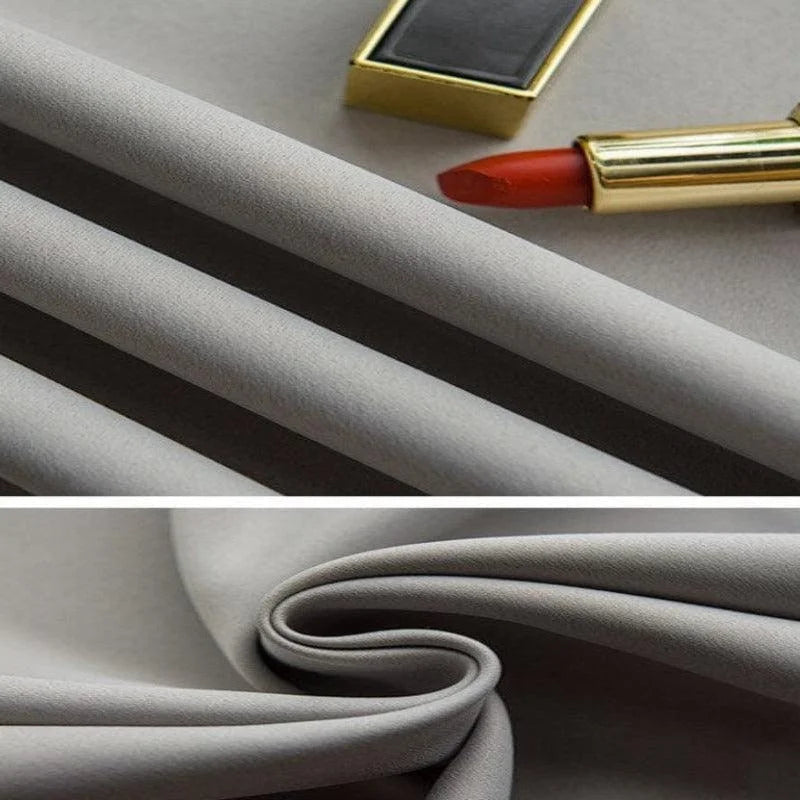 Tissu gris élégant plié et présenté sur une surface lisse, accompagné d'un rouge à lèvres et d'une boîte de maquillage, parfait pour la couture de vêtements raffinés ou la décoration intérieure moderne. Idéal pour les amateurs de mode et de design à la recherche de qualité et de style sophistiqué.