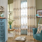 Rideaux élégants avec motifs floraux colorés pour salon moderne, ajoutant une touche de charme et de luminosité à votre intérieur. Idéal pour décorer un espace de vie accueillant et chaleureux. Coussin assorti au design floral vibrant, complétant harmonieusement la décoration du salon. Meuble et lampe bleus accentuant le style contemporain de la pièce. Vitrine et accessoire décoratif ajoutant une ambiance cosy et raffinée.