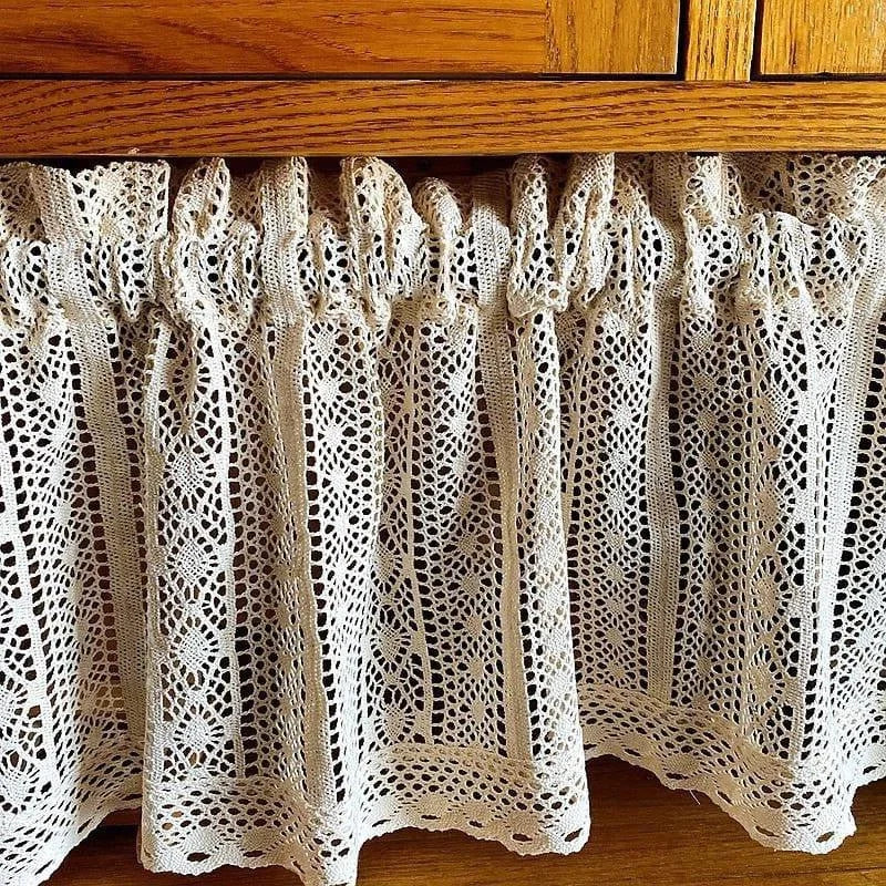 Rideau décoratif beige suspendu sous un meuble en bois, parfait pour ajouter une touche de charme vintage à votre intérieur. Idéal pour les cuisines ou les espaces nécessitant une séparation douce et esthétique. Son design ajouré évoque élégance et raffinement tout en offrant une ambiance chaleureuse et accueillante.