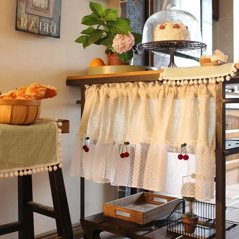 Décoration de cuisine vintage avec rideau orné de cerises, table en bois accueillant des pâtisseries sous cloche, ambiance rustique et chaleureuse pour intérieur élégant. Idéale pour créer un espace convivial et authentique.