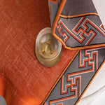 Nappe élégante avec motifs géométriques en bordure orange et grise, posée sur une table avec un verre à cocktail. Idéale pour sublimer votre décoration intérieure avec une touche de sophistication moderne. Accessoire de table parfait pour les dîners et réceptions.