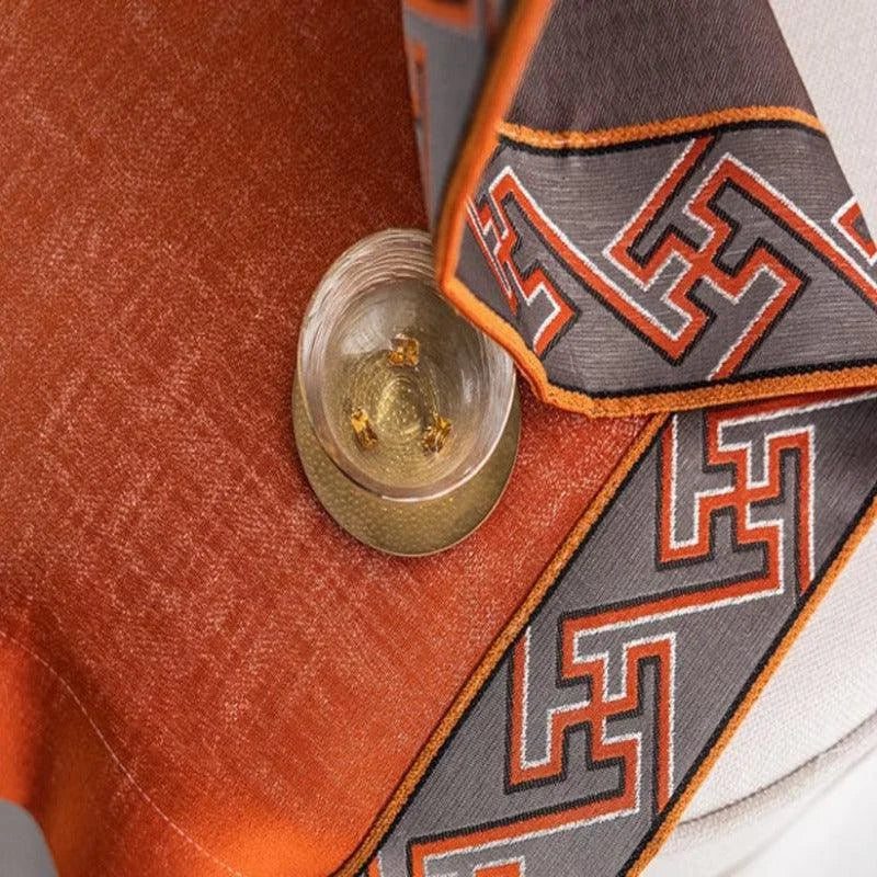 Nappe élégante avec motifs géométriques en bordure orange et grise, posée sur une table avec un verre à cocktail. Idéale pour sublimer votre décoration intérieure avec une touche de sophistication moderne. Accessoire de table parfait pour les dîners et réceptions.