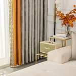 Rideaux modernes gris et orange avec motifs géométriques, ajout élégant à un salon contemporain. Accents dorés sur les tables, vase avec feuilles colorées, offrant une touche automnale. Idéal pour une décoration intérieure sophistiquée et chaleureuse.