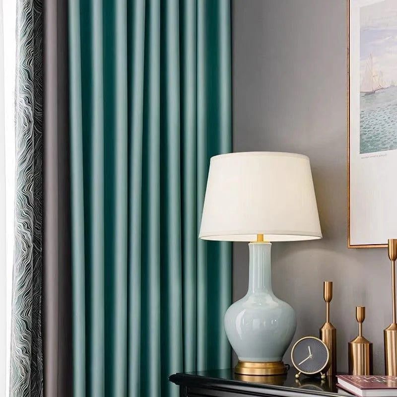 Lampe de table élégante avec abat-jour blanc, posée sur une table noire. La décoration intérieure est complétée par des rideaux verts et une horloge moderne, créant une ambiance sophistiquée et contemporaine dans un salon ou une chambre. Accessoires dorés ajoutant une touche de luxe discrète, parfaits pour rehausser l'élégance d'une pièce.
