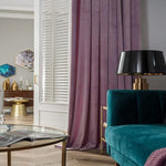 Salon moderne avec décoration élégante composée d'un rideau violet, d'un canapé vert et d'une lampe au design noir et doré. La table basse en verre ajoute une touche de sophistication tandis que les accessoires dorés complètent l'ensemble pour une ambiance chaleureuse et chic.