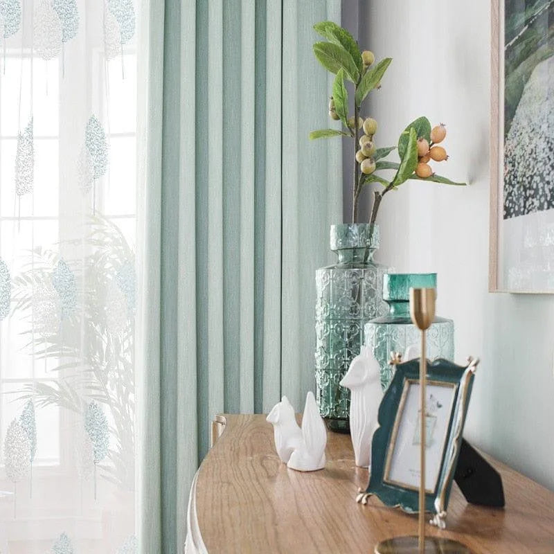 Décoration intérieure élégante avec rideaux vert menthe, vase orné et accessoires raffinés. Mettez en valeur votre salon avec cette ambiance paisible, idéale pour créer un espace de vie harmonieux. Le cadre photo et les sculptures ajoutent une touche artistique à votre meuble. Parfait pour un style moderne et accueillant.