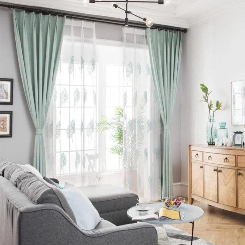 Rideaux élégants turquoise encadrant une baie vitrée dans un salon moderne et lumineux. Le style contemporain s'harmonise avec le canapé gris et la décoration de la pièce. Idéal pour ajouter une touche de sophistication et privilégier la luminosité. Parfait pour un aménagement intérieur chic et cosy.