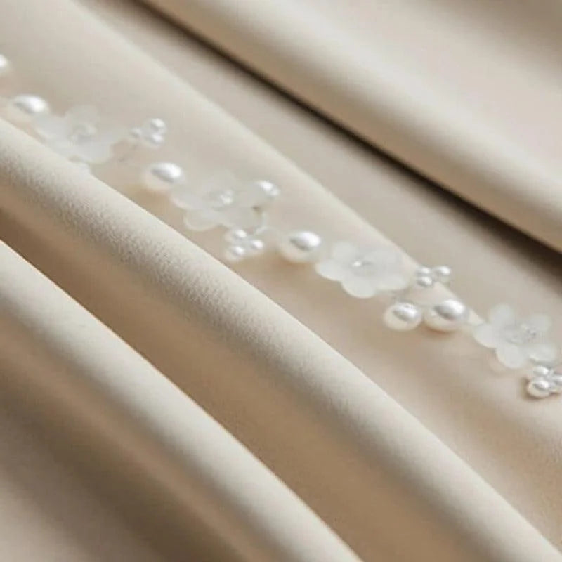 Gros plan sur un tissu délicat avec des motifs floraux et des perles. Cette image met en valeur le design élégant et sophistiqué, parfait pour les vêtements de cérémonie ou de mariage. Le contraste subtil entre le tissu lisse et les ornements ajoute une touche raffinée à l'ensemble.
