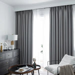 Rideaux opaques gris élégants dans un salon moderne et lumineux, avec fauteuil confortable et décorations raffinées, créant une ambiance chic et apaisante.