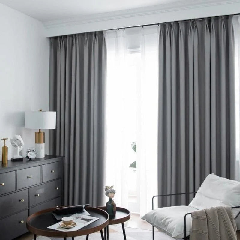 Rideaux opaques gris élégants dans un salon moderne et lumineux, avec fauteuil confortable et décorations raffinées, créant une ambiance chic et apaisante.
