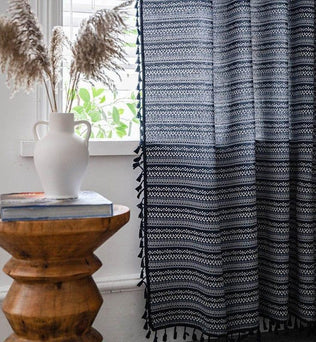 Rideau élégant à motifs géométriques noirs et blancs, suspendu dans un salon lumineux. Design chic complétant une table en bois artisanal surmontée d'un vase blanc décoratif. Idéal pour une décoration intérieure moderne et épurée.