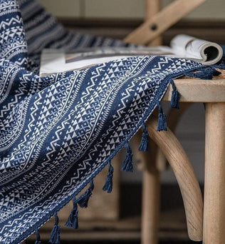 Plaid bleu à motifs géométriques sur une chaise en bois, avec franges décoratives, idéal pour une décoration intérieure cosy et chaleureuse. Ce textile ajoute une touche élégante et moderne à tout salon ou chambre à coucher. Parfait pour se draper lors des soirées fraîches.