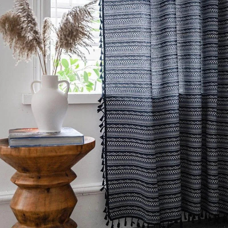 Rideau élégant à motifs géométriques noirs et blancs, suspendu dans un salon lumineux. Design chic complétant une table en bois artisanal surmontée d'un vase blanc décoratif. Idéal pour une décoration intérieure moderne et épurée.