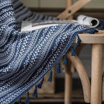 Plaid bleu à motifs géométriques sur une chaise en bois, avec franges décoratives, idéal pour une décoration intérieure cosy et chaleureuse. Ce textile ajoute une touche élégante et moderne à tout salon ou chambre à coucher. Parfait pour se draper lors des soirées fraîches.