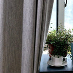 Rideau moderne gris dans un salon lumineux, avec une plante d'intérieur et une tasse sur une table à proximité d'une fenêtre en arrière-plan. Idéal pour créer une ambiance chaleureuse et intime. Parfait pour un intérieur contemporain et élégant.