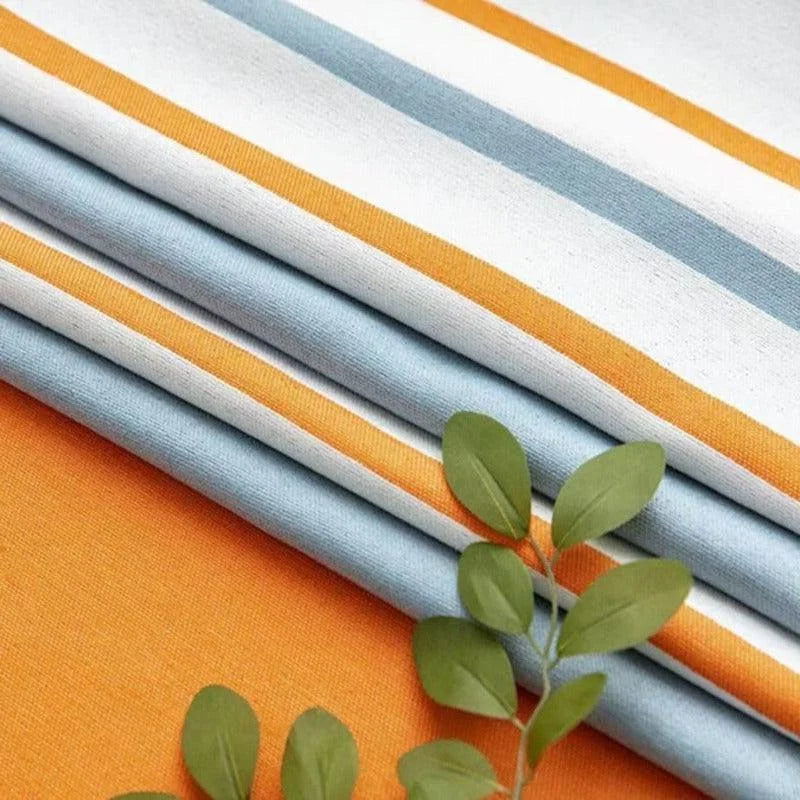 Empilement de tissus à rayures colorées bleu, blanc et orange, avec une décoration de feuillage vert, parfait pour l'artisanat et la décoration intérieure. Idéal pour des projets créatifs ou pour ajouter une touche vibrante à n'importe quel espace.