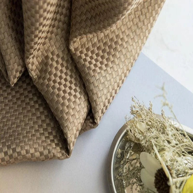 Tissu décoratif avec motif tissé brun, présenté sur une surface claire avec un arrangement floral minimaliste. Parfait pour ajouter une touche de sophistication et de naturel à votre intérieur. Design élégant et intemporel avec des accents naturels.