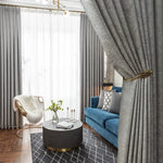 Salon moderne et élégant avec rideaux gris, canapé bleu, table basse ronde et chaise design. Le tapis à motifs géométriques ajoute une touche contemporaine. Idéal pour un intérieur chic et confortable.