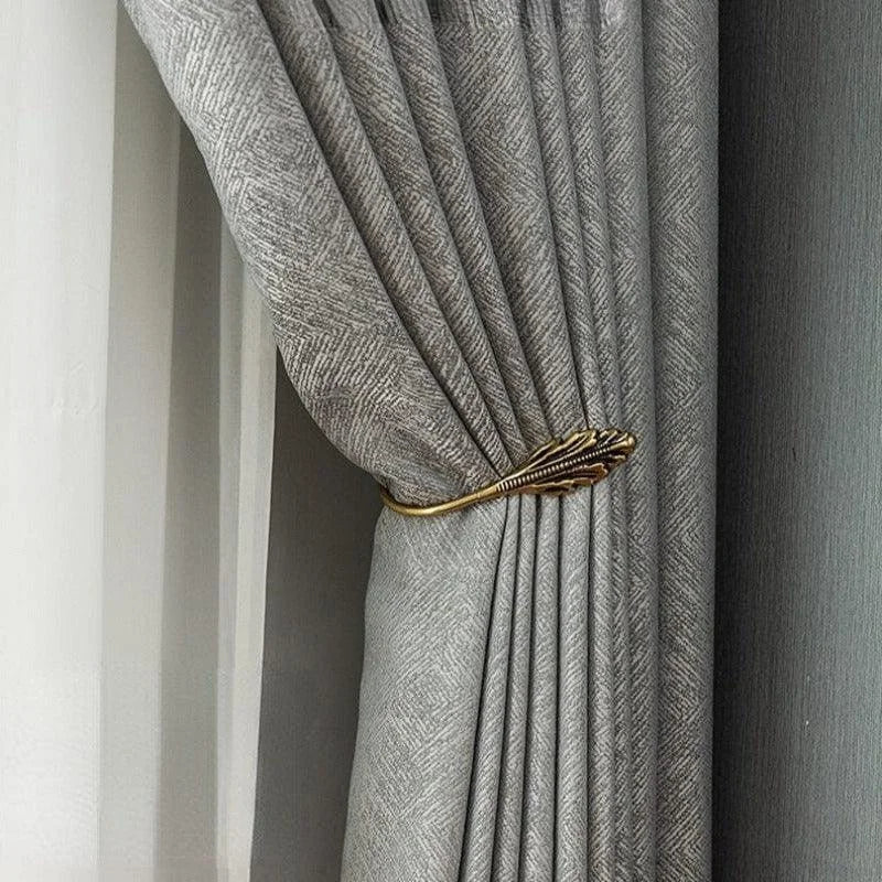 Rideau élégant de couleur grise avec motif discret, retenu par un embrasse doré en forme de feuille, idéal pour une décoration intérieure raffinée et moderne. Convient parfaitement pour les salons ou chambres à la recherche d'une touche de sophistication.