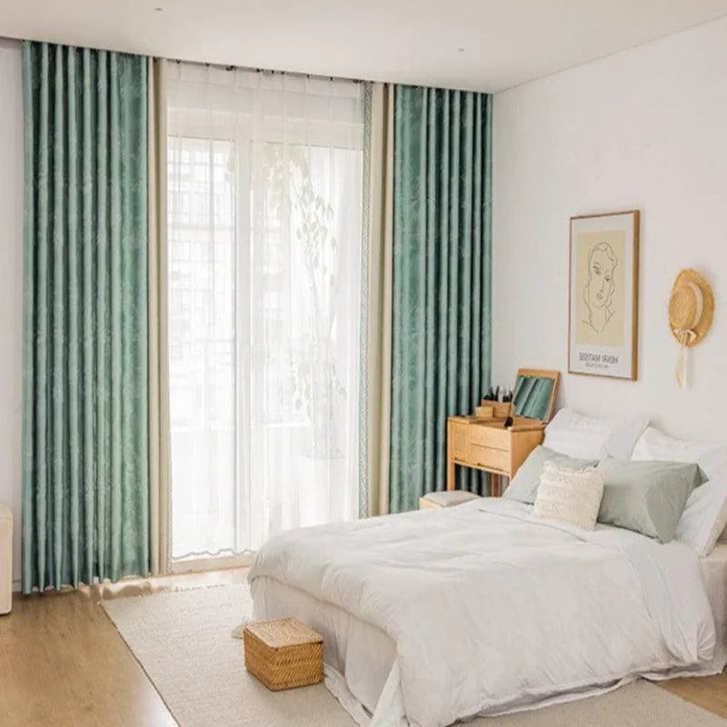 Chambre à coucher moderne avec rideaux bleu-vert, grande fenêtre laissant entrer la lumière naturelle. Lit confortable avec literie blanche, table de maquillage en bois et décoration murale minimaliste. Ambiance sereine et épurée pour un espace de repos idéal.