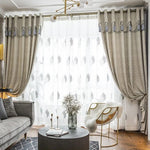 Chambre élégante avec rideaux opaques gris et voilage à motifs, apportant une ambiance chaleureuse et moderne. Complètement intégrés dans un salon chic avec un canapé gris, un fauteuil design et une table basse noire, ces rideaux améliorent l'esthétique de l'espace. Leur suspension en anneaux ajoute une touche de sophistication. Parfait pour une décoration intérieure contemporaine et tendance.