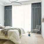 Chambre moderne avec rideaux opaques gris offrant une ambiance apaisante. Chambre à coucher lumineuse dotée d'une grande fenêtre et d'un lit confortable. Espace de vie élégant avec décoration épurée et chaise design. Parfait pour améliorer l'intimité et le confort de votre intérieur. Idéal pour un style contemporain et cosy.