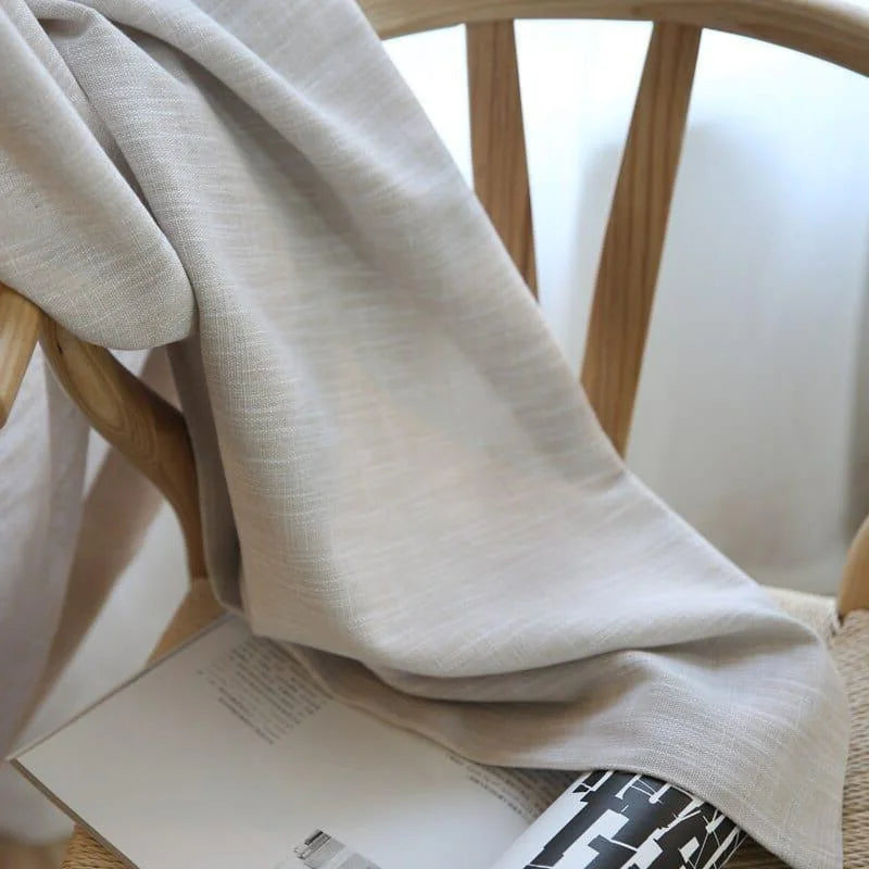 Élégante couverture beige soigneusement drapée sur une chaise en bois clair, avec un livre ouvert à proximité. Idéale pour un intérieur moderne, cette pièce apporte une touche de sophistication et de confort à votre espace de vie.