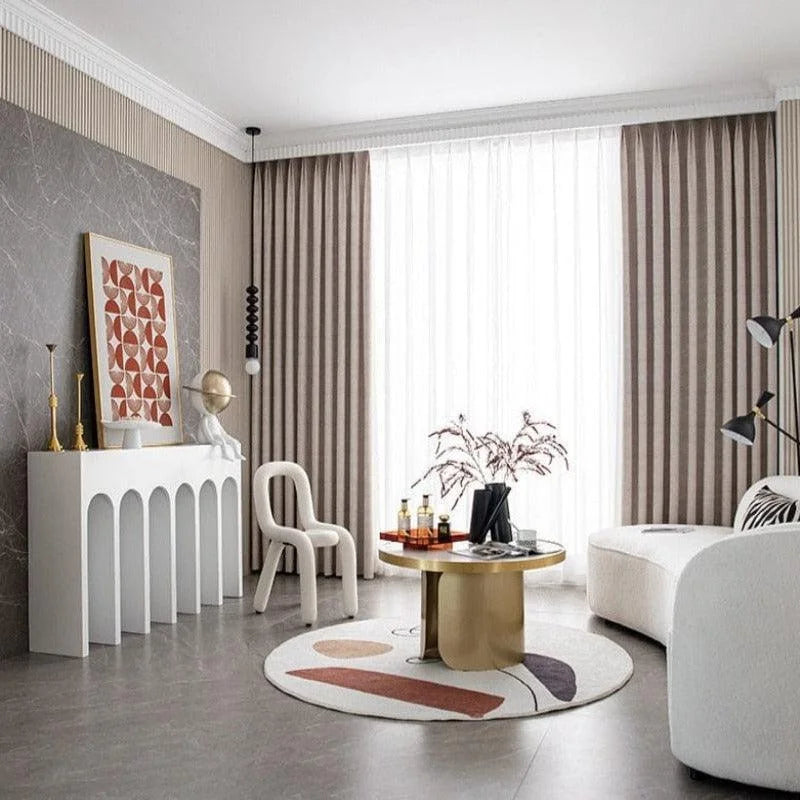 Salon moderne avec décoration élégante, mettant en avant un design contemporain. Mobilier design avec table basse circulaire dorée et canapé aux lignes courbes. Suspension lumineuse tendance et rideaux rayés apportant une touche sophistiquée.éléments décoratifs artistiques sur une console blanche en avant-plan.