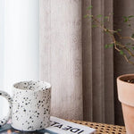 Tasse à motifs sur une table en osier à côté d'une plante en pot et de rideaux, créant une ambiance chaleureuse et moderne dans un intérieur lumineux. Parfait pour une décoration élégante et tendance.